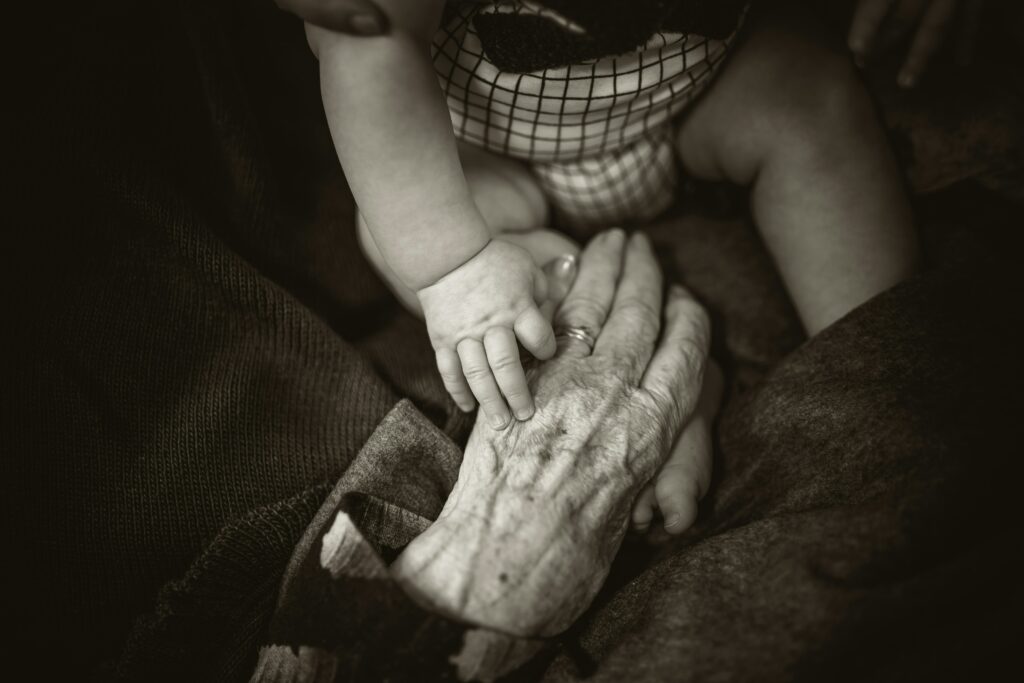 Main de bébé tenant la main d'une personne âgée. Photo par Rod Long, Unsplash.